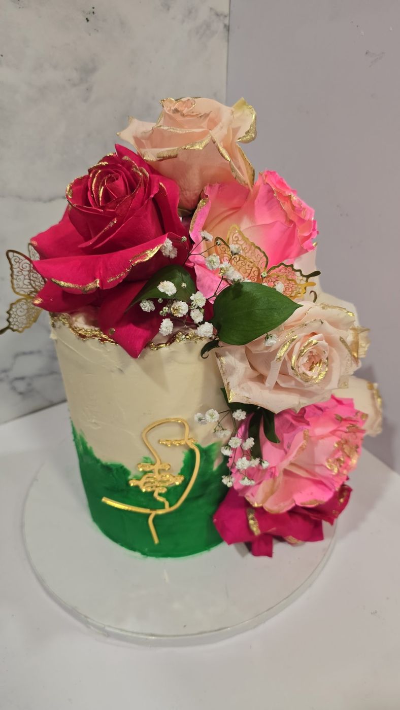 Cream and green cake topped with pink and red roses and a gold butterfly